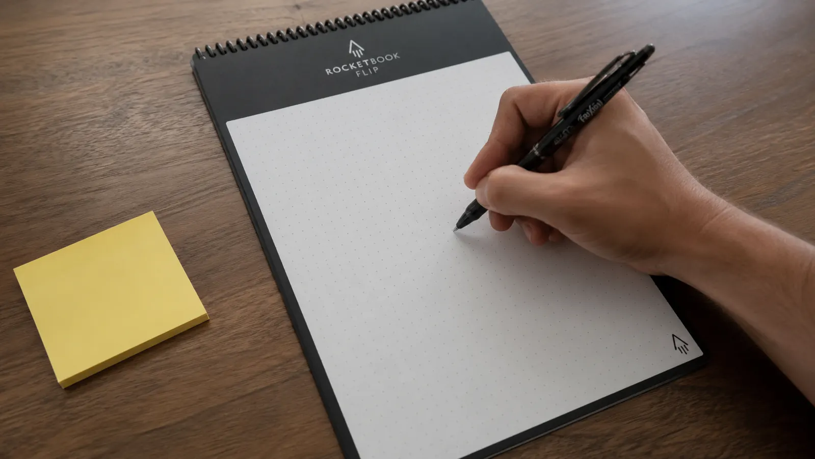 Hand writing a to-do list on a Rocketbook Flip page next to a small stack of loose sticky notes for comparison