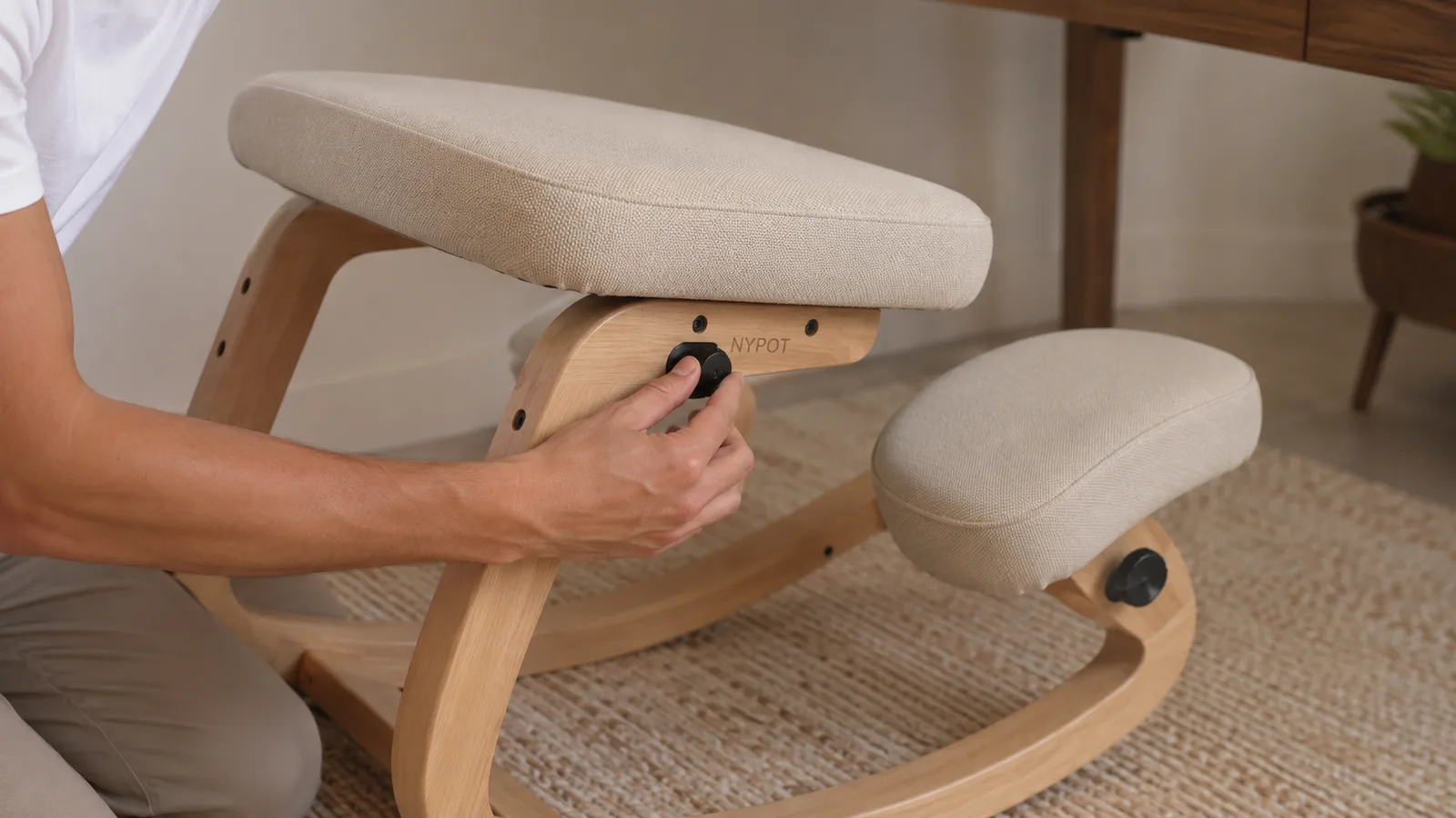 Close-up of hands adjusting the seat angle lever on a black ergonomic kneeling chair beside a desk