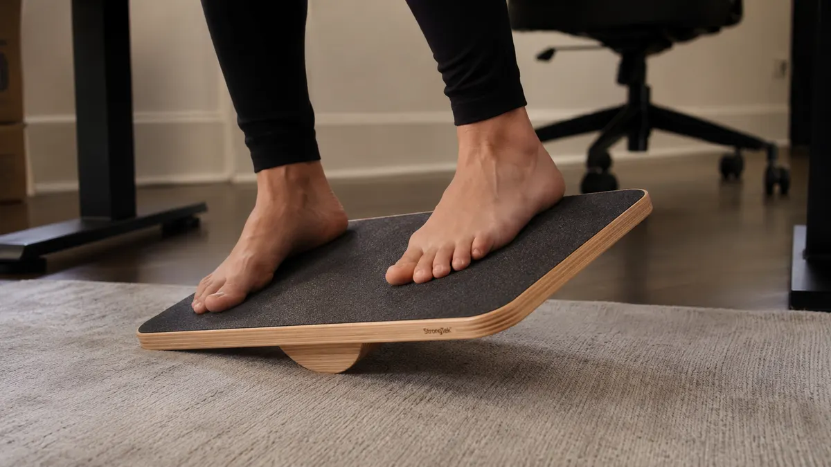 Close-up of feet balanced on a StrongTek wooden balance board under a standing desk